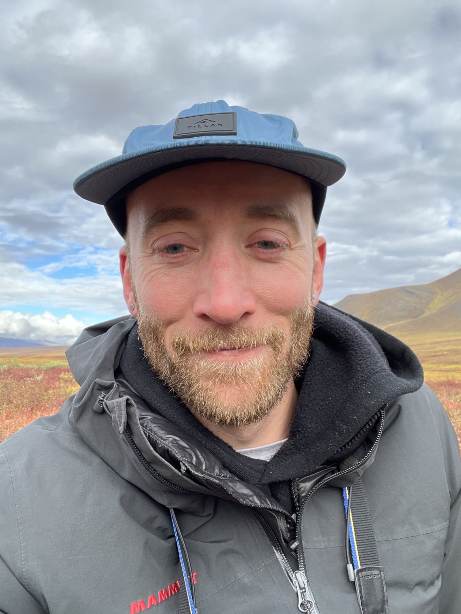 Selfie portrait of Alex in hat and coat standing in the tundra of the Brooks Range in fall.